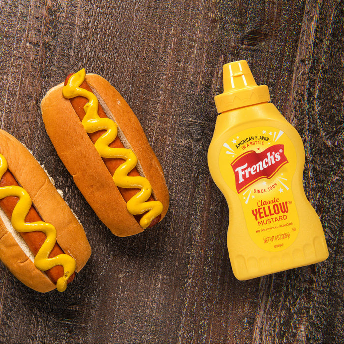 ["Two hot dogs with mustard and a bottle of French's Classic Yellow Mustard."]