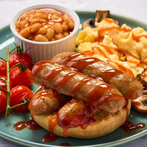 A hearty breakfast plate features sausages on a toasted muffin and scrambled eggs drizzled with Frank'S Redhot Franks Squeeze Tangy Bbq 354 Ml alongside baked beans and vine tomatoes.