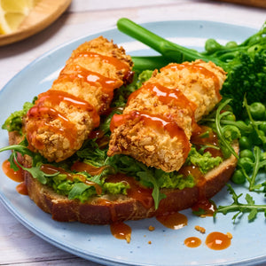 Two crispy breaded fish fillets are drizzled with Frank'S Squeeze Sticky Sweet 354 Ml sauce and served on a slice of toasted sourdough bread with mashed peas and arugula.