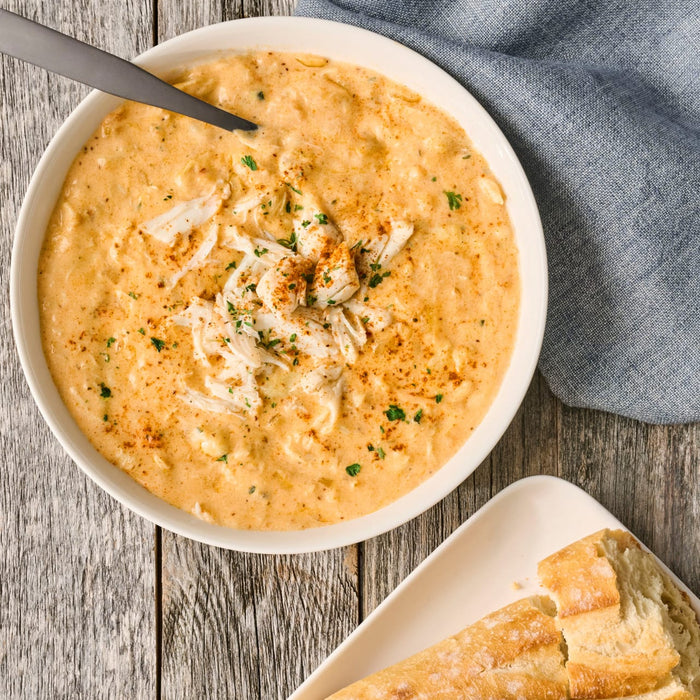A bowl of creamy crab soup garnished with crab meat and parsley, served with crusty bread.