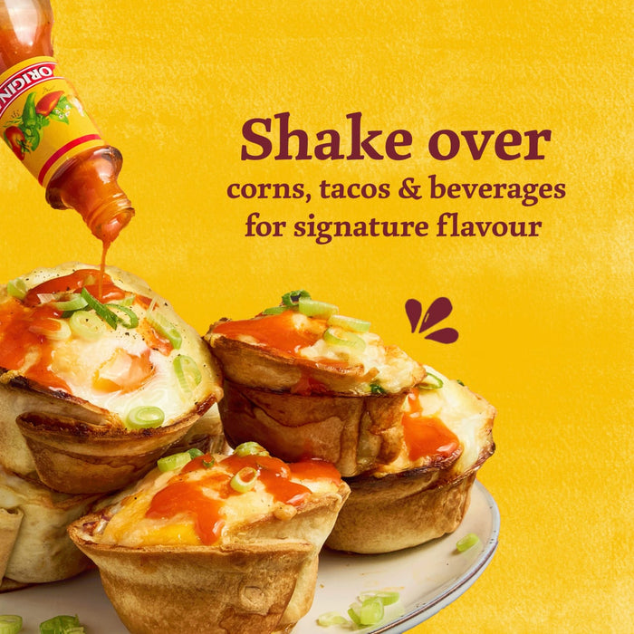 A bottle of Cholula Original Mexican Hot Sauce 150Ml is being drizzled over a stack of savory breakfast egg cups topped with green onions against a bright yellow background.