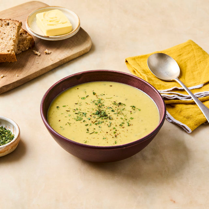 A comforting bowl of creamy yellow soup is garnished with herbs and served with a side of bread and butter.