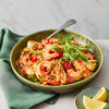 A rustic green bowl is filled with creamy shrimp and tomato linguine, garnished with fresh arugula and served with a side of lemon wedges.