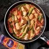 A pan of creamy chicken curry with red peppers and sugar snap peas is shown next to a container of Schwartz Medium Curry Powder 90G.