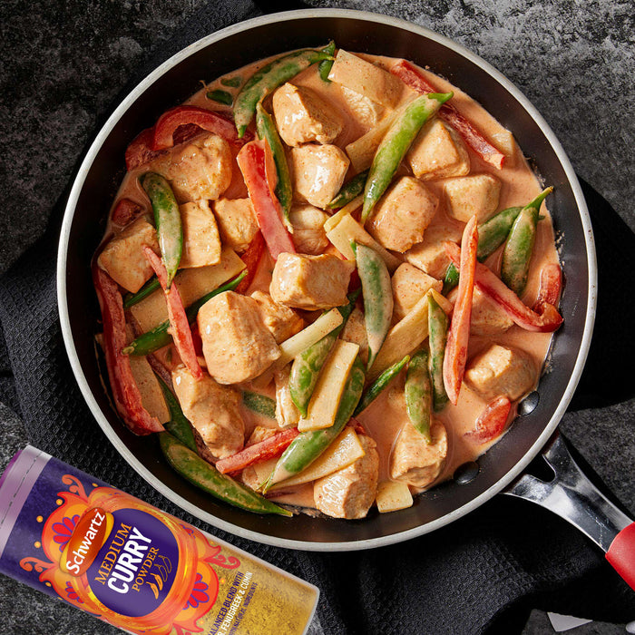 A pan of creamy chicken curry with red peppers and sugar snap peas is shown next to a container of Schwartz Medium Curry Powder 90G.
