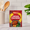 A packet of Schwartz Chicken Chasseur Recipe Mix 40G is displayed on a marble countertop in a bright kitchen setting with cooking utensils and a plant in the background.