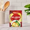 A single packet of Schwartz Hollandaise Sauce Mix 25G is set in a bright kitchen scene on a marble countertop, ready to be prepared.