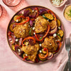 Roasted chicken thighs and colorful vegetables are seasoned to perfection with Schwartz Cajun Seasoning 110G and served on a pink plate with a side of feta cheese and creamy dip.