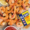 A platter of seasoned shrimp and a lemon wedge are served with cocktail sauce and a tin of Old Bay Seasoning.