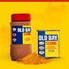 A large plastic container and a classic metal tin of Old Bay Seasoning stand behind a small mound of the iconic spice blend against a vibrant yellow background.