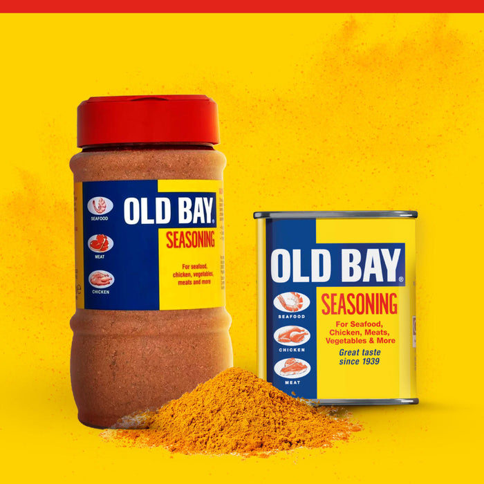 A large plastic container and a classic metal tin of Old Bay Seasoning stand behind a small mound of the iconic spice blend against a vibrant yellow background.