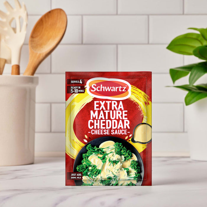 A packet of Schwartz Extra Mature Cheddar Cheese Sauce 30G is shown on a kitchen counter, with a serving suggestion of the sauce over broccoli on the front.