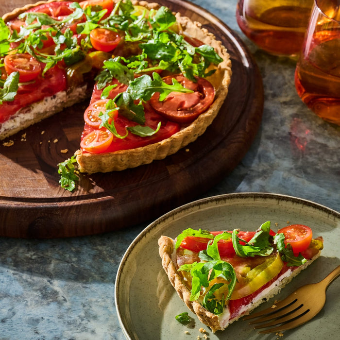 A slice of fresh tomato and arugula tart sits on a plate next to a golden fork, showcasing the vibrant colors and textures that could be inspired by a Spice Rack Engraved Gift Set.
