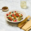 A fresh Greek salad featuring cucumbers, tomatoes, olives, and feta cheese is beautifully presented alongside a glass of water and a small bowl of dressing belonging to the Spice Rack Engraved Gift Set.