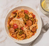 A bowl of chicken and sausage jambalaya seasoned with Schwartz Extra Spicy Cajun 42G Grill&Sizzl sits on a marble surface next to a glass of lemon water.