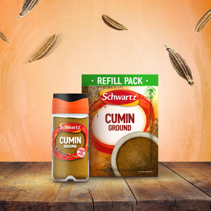 A jar of Schwartz Cumin Ground 37G and its corresponding refill pack sit on a rustic wooden table, with whole cumin seeds floating in the warm-toned background.