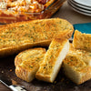 A freshly baked loaf of garlic bread, sliced and ready to serve alongside a pasta bake, is generously seasoned with what could be Schwartz Garlic Granules 50G for a savory flavor.
