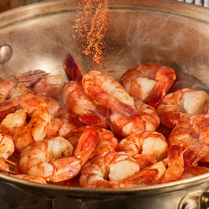 A generous amount of Schwartz Paprika 40G is sprinkled over steaming shrimp cooking in a large metal pan.