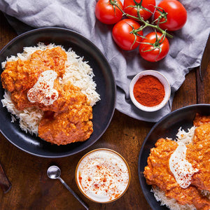 A delicious meal of chicken paprikash is served in two bowls, with a small bowl of Schwartz Paprika 40G and fresh tomatoes on the side.
