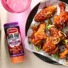 A bottle of Schwartz Af Sy Korean Seas sits next to a plate of crispy air fried chicken wings glazed in a spicy sauce and topped with sesame seeds and spring onions.