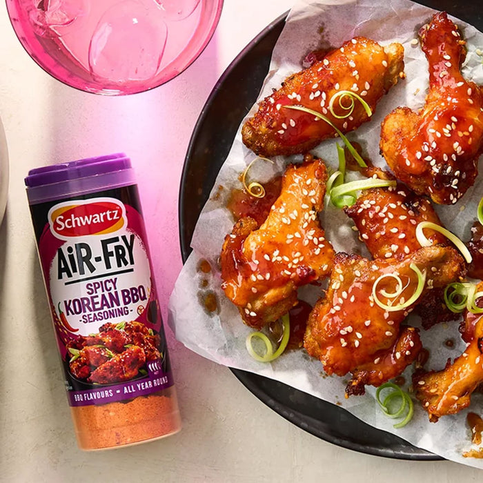 A bottle of Schwartz Af Sy Korean Seas sits next to a plate of crispy air fried chicken wings glazed in a spicy sauce and topped with sesame seeds and spring onions.