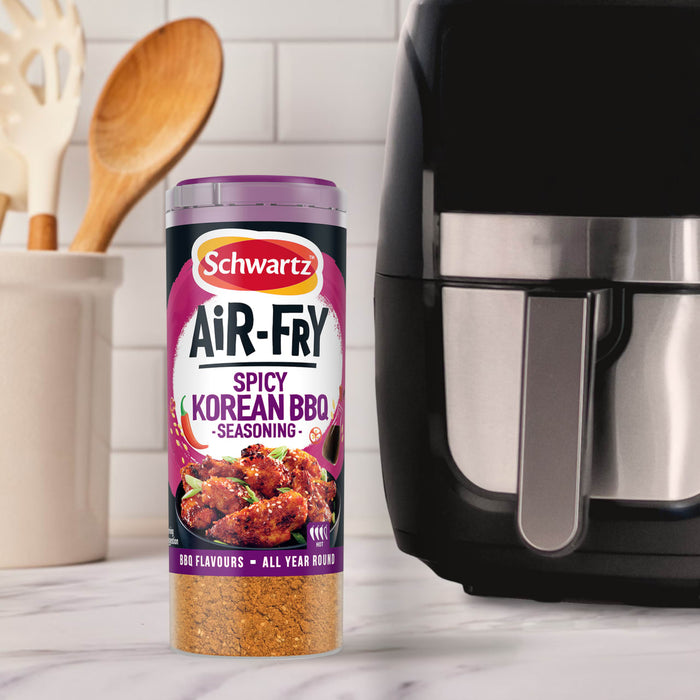 A container of Schwartz Af Sy Korean Seas stands on a marble countertop next to a black air fryer and kitchen utensils.