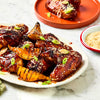 A platter of glazed chicken wings and grilled pear wedges seasoned with Schwartz Af Sy Korean Seas and garnished with sesame seeds and sliced green onions.