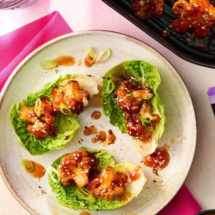 A plate of roasted cauliflower lettuce wraps seasoned with Schwartz Af Sy Korean Seas and garnished with sesame seeds and sliced spring onions.