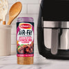 A bottle of Schwartz Af Chinese Cs Sea stands on a marble countertop next to a black air fryer and a jar of wooden utensils.