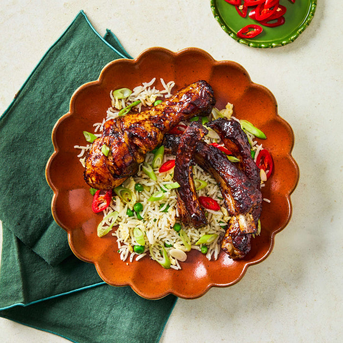 A top-down view of a plate featuring glazed chicken and ribs prepared with Schwartz Af Chinese Cs Sea served over a bed of egg fried rice with peas and spring onions.