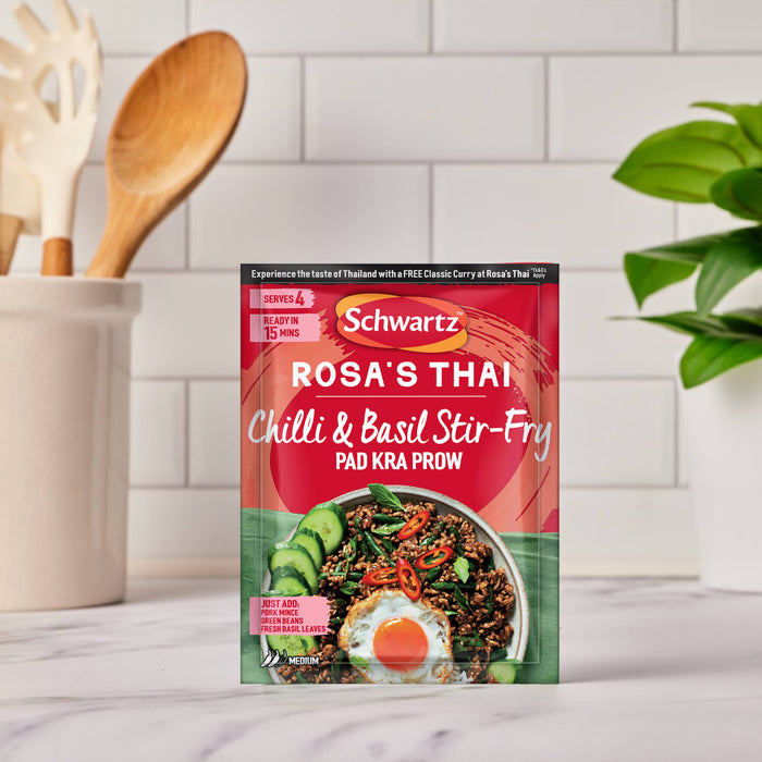 A red packet of Sa Rt Chili Basil Stir Fry X12 sits on a kitchen counter, showing a serving suggestion of the Thai dish with a fried egg.