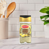 A bottle of Schwartz Jr Lemon Pepper Seas X6 stands on a marble countertop in a bright kitchen setting with wooden utensils and a green plant in the background.