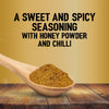 A wooden spoon holds a mound of Jr Hot Honey Seas X6 over a rustic wooden table against a gold background with text describing it as a sweet and spicy seasoning with honey powder and chilli.