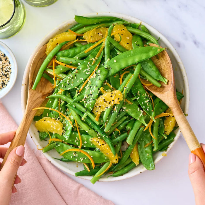 A vibrant green bean and snow pea salad is tossed with orange segments and a sprinkle of Jr Every Bagel Seas X6 for added texture and flavor.