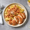 A plate of penne pasta and sliced chicken breast is topped with a creamy tomato sauce seasoned with Schwartz Basil 10G.