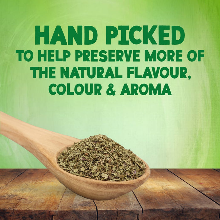 A wooden spoon filled with dried herbs rests on a rustic table to highlight that Schwartz Basil 10G is hand picked to help preserve more of the natural flavour colour and aroma.