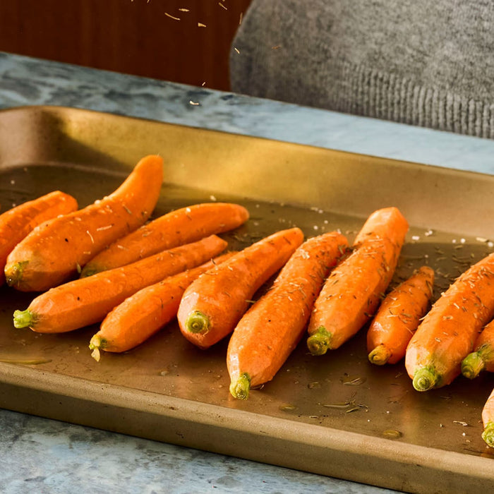Carrots on a baking sheet are being seasoned with Schwartz Thyme 11 G before being roasted.