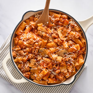 A large skillet filled with rigatoni pasta, mushrooms, and a hearty meat sauce is perfectly seasoned with Schwartz Spicy Italian Seasoning, 42G and topped with shredded cheese.