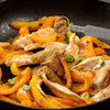 A metal measuring spoon sprinkles Schwartz Ground Ginger 26G Jar over a sizzling pan of chicken strips and orange bell peppers.