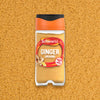 A Schwartz Ground Ginger 26G Jar is centered against a textured background of the same fine golden spice powder.