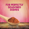 A wooden spoon overflowing with Schwartz Salt, Paprika & Pepper Season All Seasoning 70G rests on a rustic wooden table against a pink textured background with the text FOR PERFECTLY SEASONED DISHES.