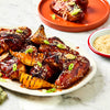A platter of glazed chicken wings and grilled pear wedges is garnished with sesame seeds and green onions after being prepared with Schwartz Classic Bbq Seasoning 44G.