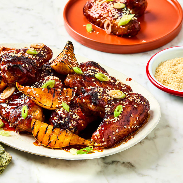 A platter of glazed chicken wings and grilled pear wedges is garnished with sesame seeds and green onions after being prepared with Schwartz Classic Bbq Seasoning 44G.