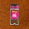 A jar of Schwartz Classic Bbq Seasoning 44G is centered against a background of the loose reddish brown spice blend.
