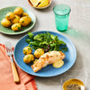 A plated meal of grilled salmon with a creamy sauce, new potatoes, and a fresh green salad, with a small bowl of cracked black pepper nearby.