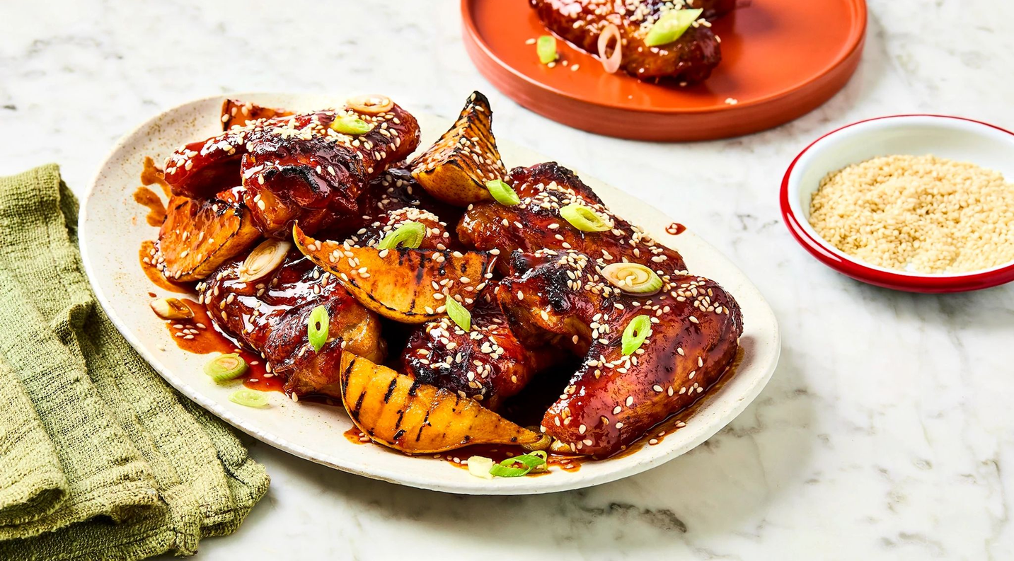 Plated dish of teriyaki chicken with vegetables on a marble surface, accompanied by a small bowl of sesame seeds.