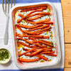 A metal baking dish is filled with freshly roasted and glazed carrots, garnished with herbs and spices.
