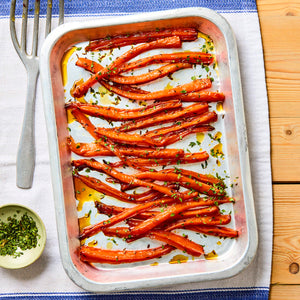 A metal baking dish is filled with freshly roasted and glazed carrots, garnished with herbs and spices.