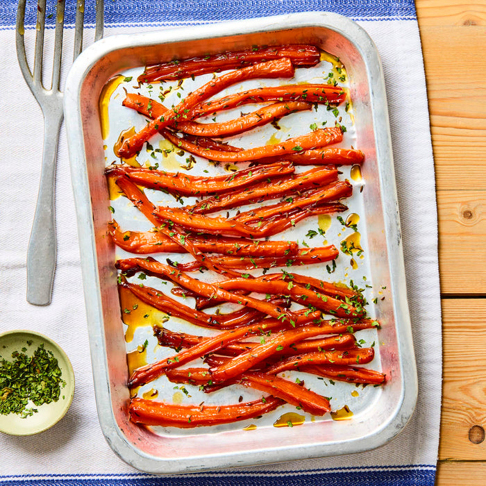 A metal baking dish is filled with freshly roasted and glazed carrots, garnished with herbs and spices.