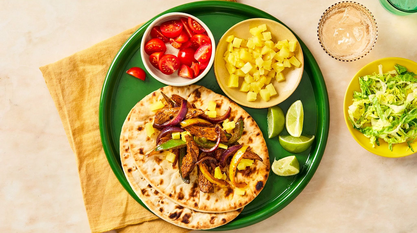 Green tray with tortillas, vegetables, and sauces on a beige surface